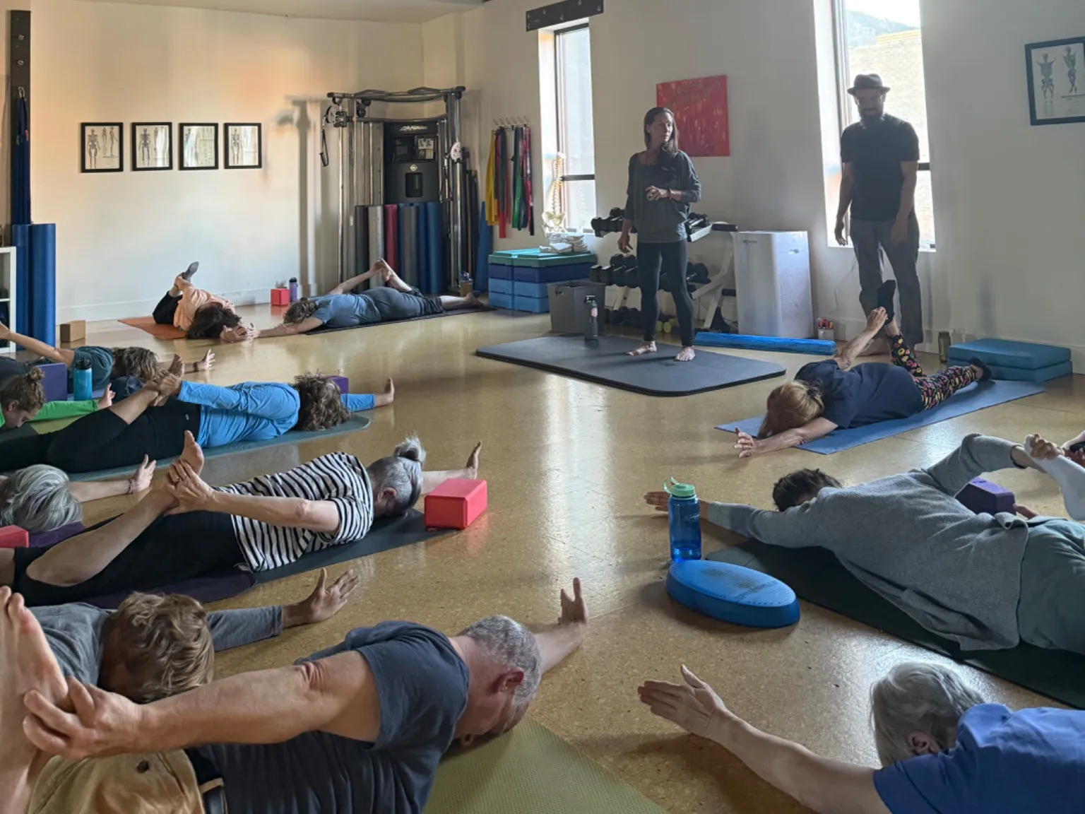 Participants lie on mats in a myofascial release stretch while two instructors guide the room at the Breath Reboot workshop in Boulder